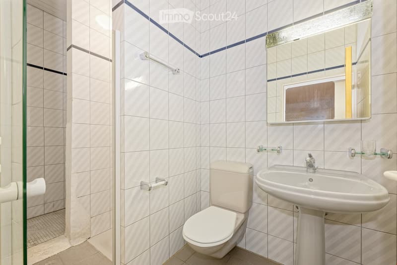 Modern bathroom with white tiles, a toilet, a sink with a faucet, and a mirror above the sink. The walls feature a decorative blue diagonal stripe pattern.