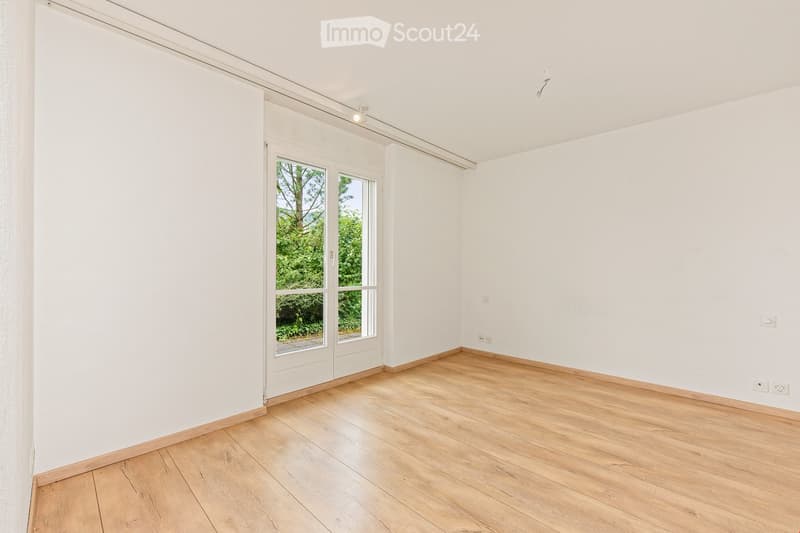 Empty room with white walls, wooden flooring, and a large window with white frame. No furniture or equipment present.