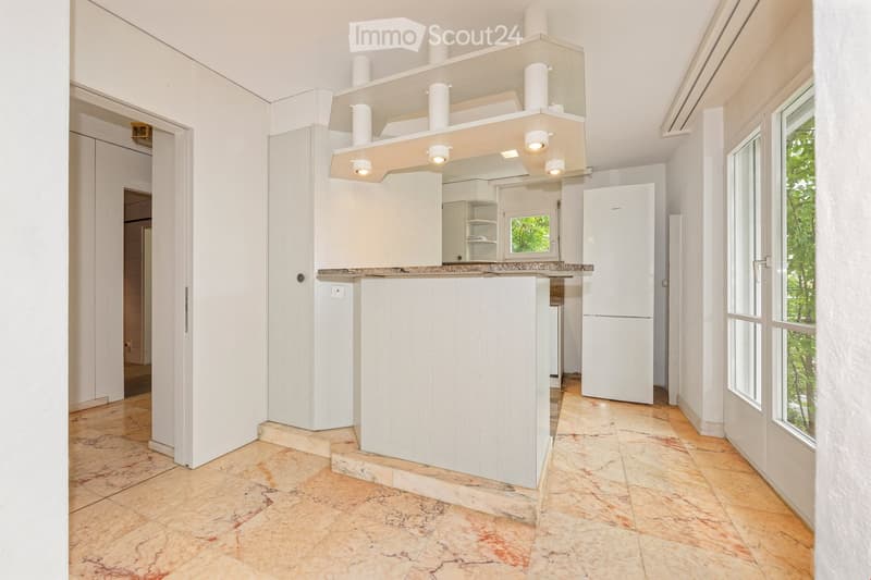 Modern kitchen with white cabinets, a central island, and a refrigerator. The space features a marble countertop and tiled flooring.