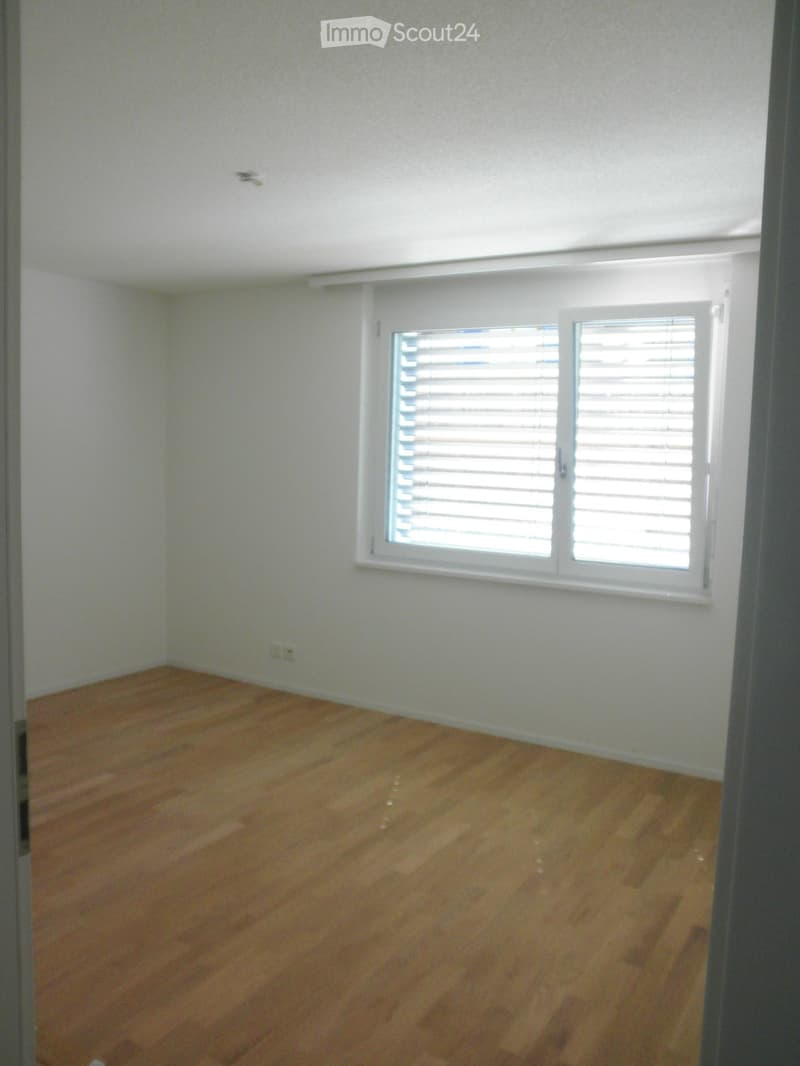 Empty room with light-colored walls and wooden flooring, featuring a single window with blinds.