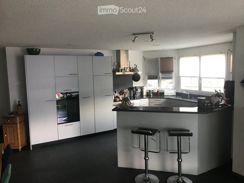 Modern kitchen with white cabinets, black countertops, and a central island with two stools. The kitchen features a sink, oven, and various appliances.