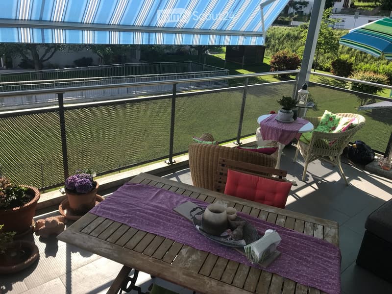 Balcony with a wooden table, chairs, and potted plants, featuring a purple table runner and a cup on the table.