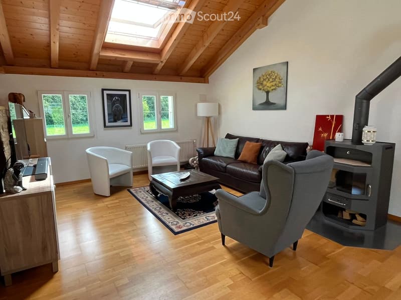 Bright living room with wooden floors, a dark leather sofa, a coffee table, armchairs, a fireplace, and artwork on the walls.