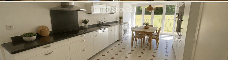 Modern kitchen with white cabinets, black countertops, a sink, dishwasher, washing machine, and a small dining area with a table and chairs. The space features a range hood, potted plants, and a view of a balcony through large windows.