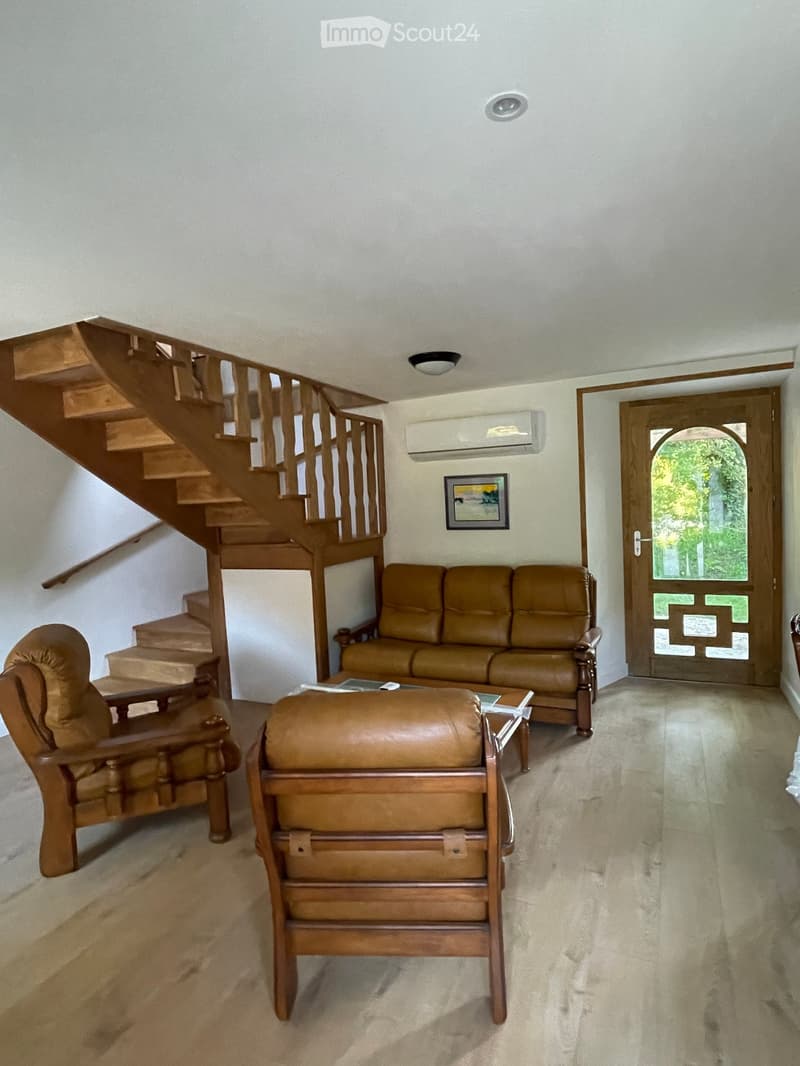 Living room with a brown leather sofa, ottoman, armchair, coffee table, and a staircase leading to an upper level.