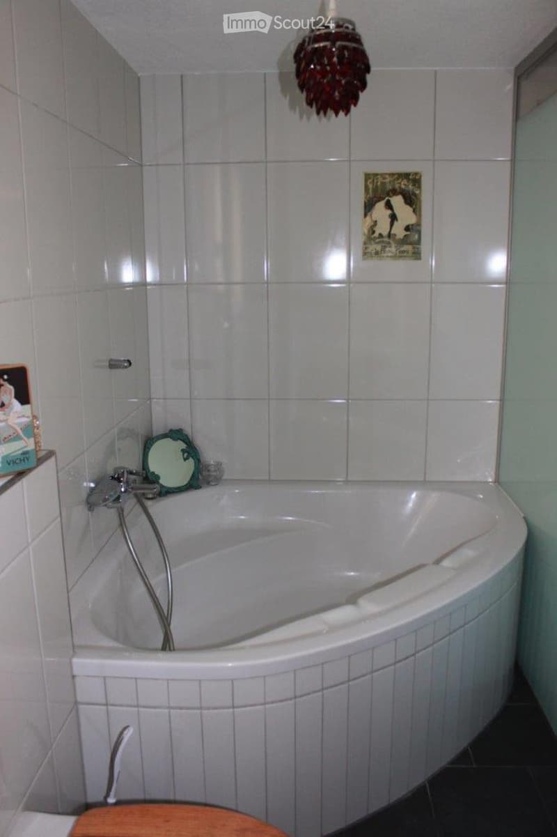 Bathroom with a white bathtub, a small mirror, a wooden stool, and a decorative chandelier.