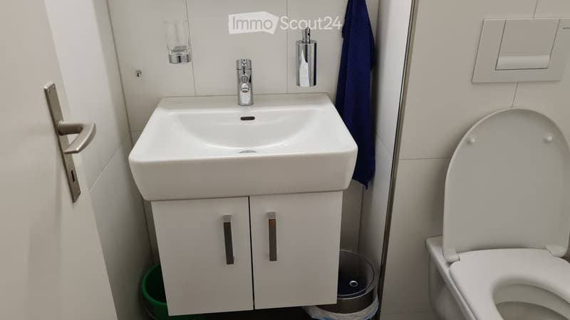 Modern bathroom with a white sink, chrome faucet, mirrored cabinet, toilet, and a blue towel hanging on the wall.