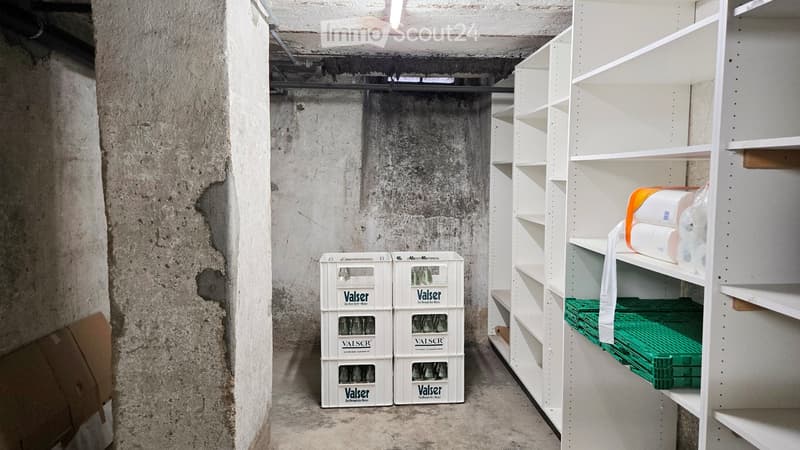 Empty storage room with concrete walls, white shelving unit, and stacked white boxes labeled "Valser" on the floor.