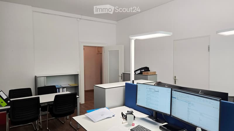 Office space with desks, chairs, multiple computer screens, and office supplies.