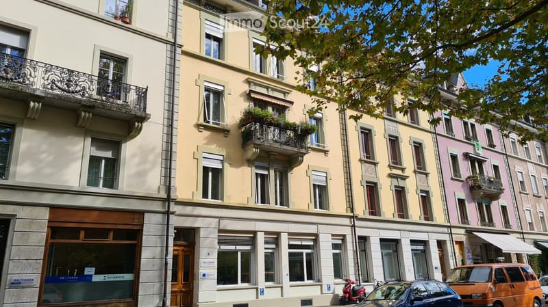 Multi-story residential building with balconies, large windows, and a storefront at the ground level.