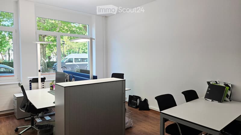 Modern office space with large windows, desks, chairs, a screen, a lamp, and a cabinet.