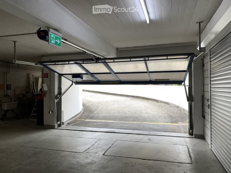 Underground garage with a large, open automatic door leading to an outdoor area. The space is clean and well-lit with fluorescent lighting.