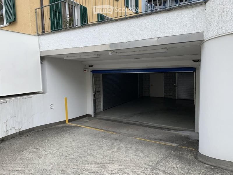 Underground garage with multiple parking spaces, white walls, and a blue overhead door.