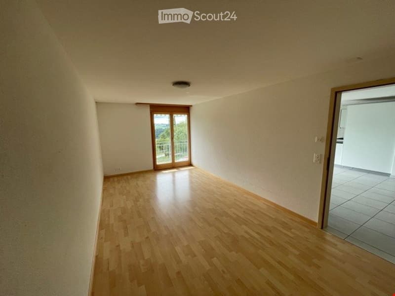 Empty room with wooden flooring, white walls, and a sliding glass door leading to a balcony.