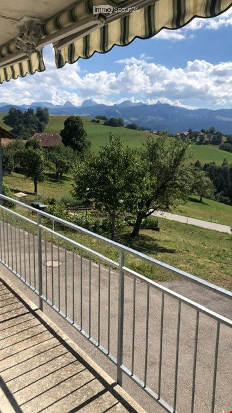Balcony with metal railing, overlooking a green landscape with trees and mountains in the background.