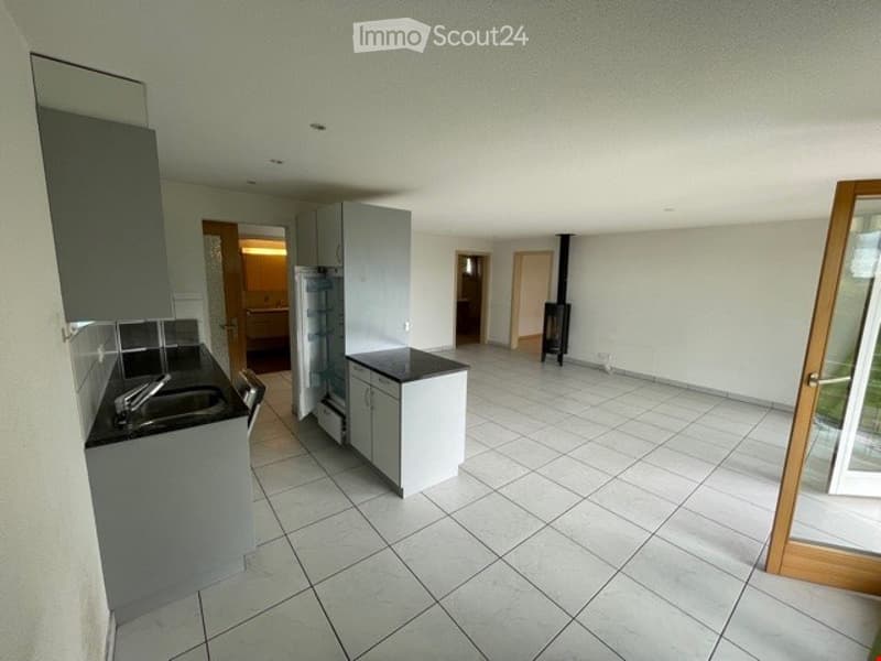 Empty kitchen with tiled floor, grey cabinets, sink, and a visible fireplace in the background.