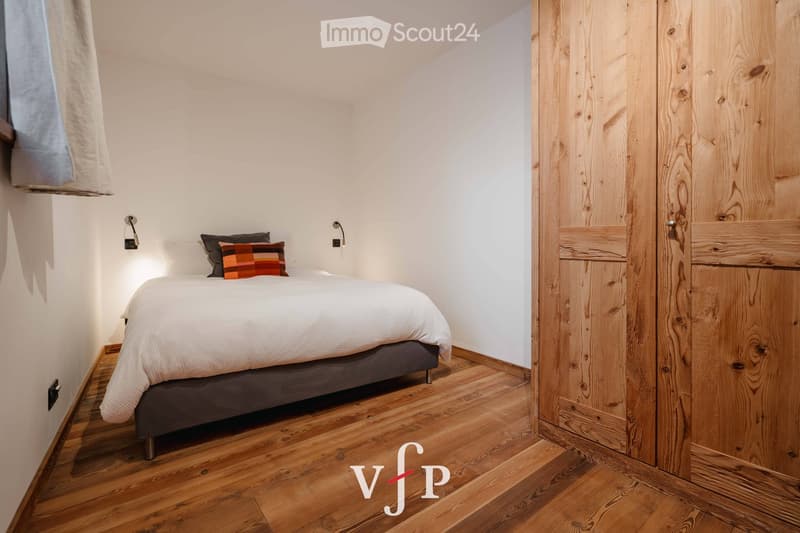 Cozy bedroom with a neatly made bed, wooden wardrobe, and warm lighting.