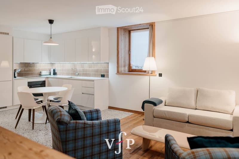 Modern open-plan living and dining area with a sofa, armchair, coffee table, dining table with chairs, and a kitchen area with cabinets and an oven.