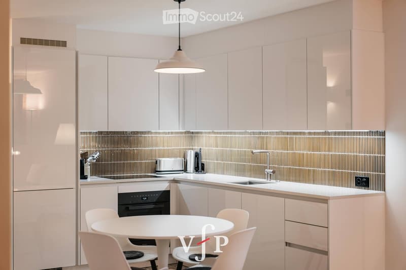 Modern kitchen with white cabinets, stainless steel appliances, and a white dining table with chairs.