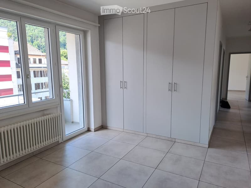 Empty room with tiled floor, white walls, large built-in wardrobes, and a window with a view of the street.