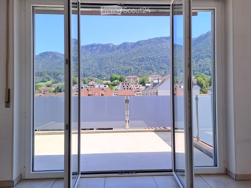 Open sliding glass doors lead to a balcony with a scenic mountain and town view.