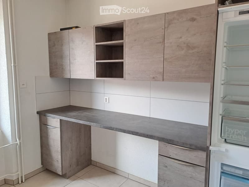 Modern kitchen with light wood cabinets, a gray countertop, and a stainless steel refrigerator.