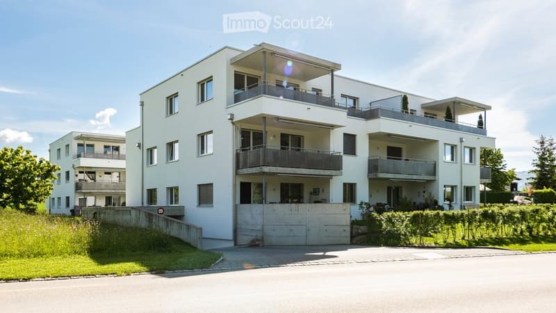 Modern multi-story residential building with white exterior, multiple balconies, and a garage entrance.
