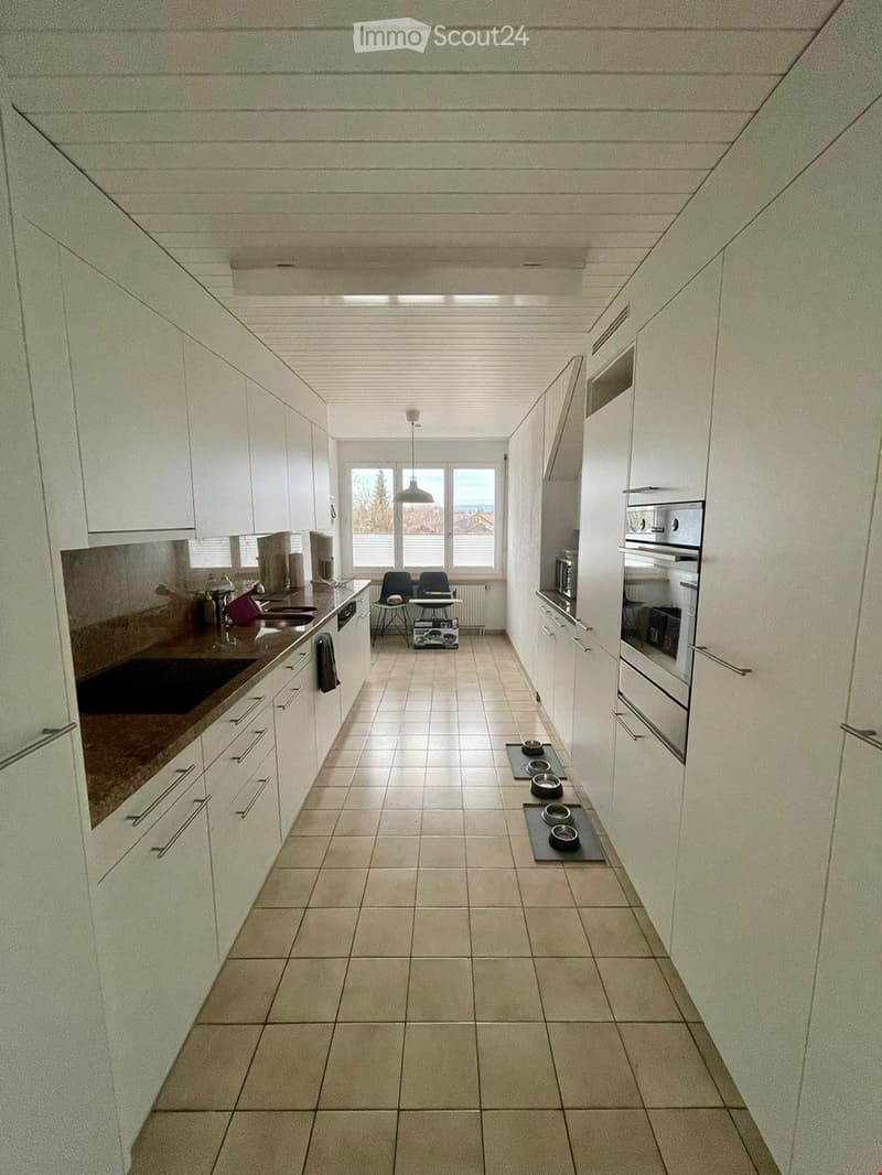 Modern kitchen with white cabinets, tiled floor, and stainless steel appliances. Includes a sink, oven, microwave, and a small table with chairs.