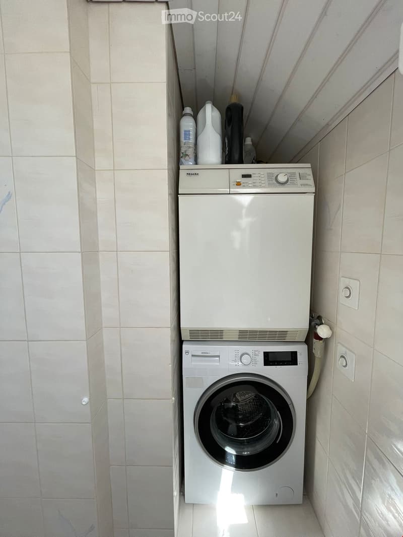 A compact bathroom area featuring a stacked washing machine and dishwasher unit with detergent bottles placed on top.