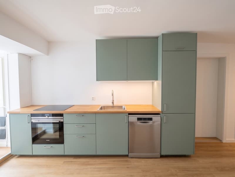 Modern kitchen with light green cabinets, wooden countertops, stainless steel appliances, and a sink with a faucet.