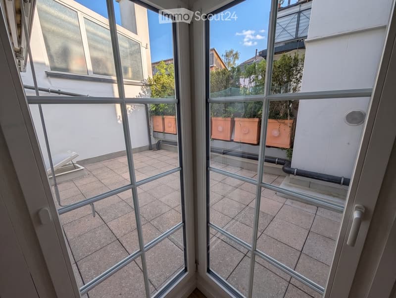 Balcony with tiled floor, glass railing, and several terracotta planters with greenery.