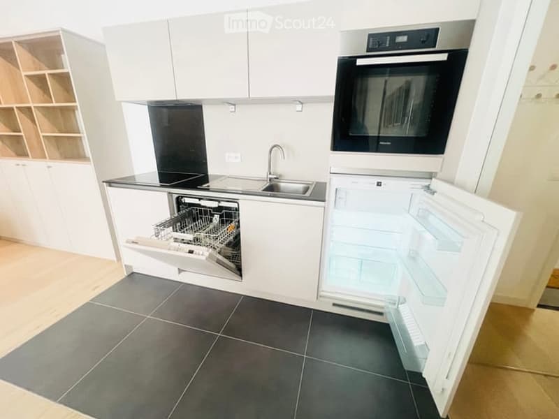 Modern kitchen with white cabinets, stainless steel appliances, and dark tiled flooring. The refrigerator and dishwasher are open, revealing their interiors.