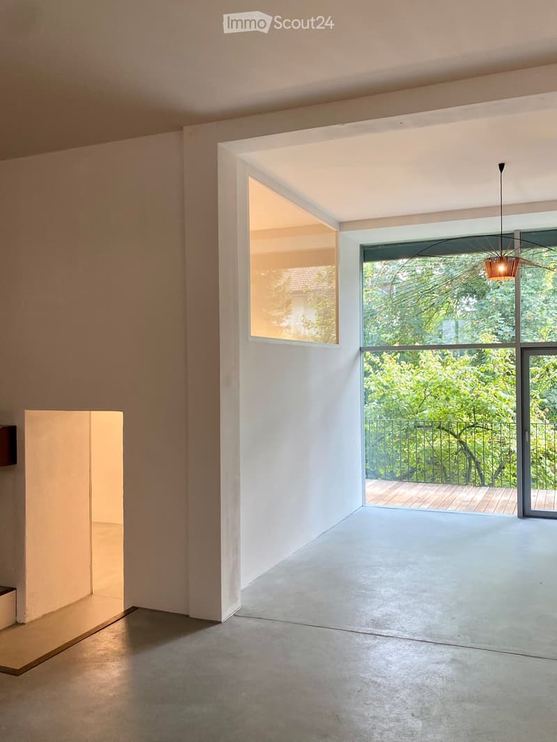 Empty room with large windows and a balcony, featuring a modern, minimalist design with concrete floors and white walls.