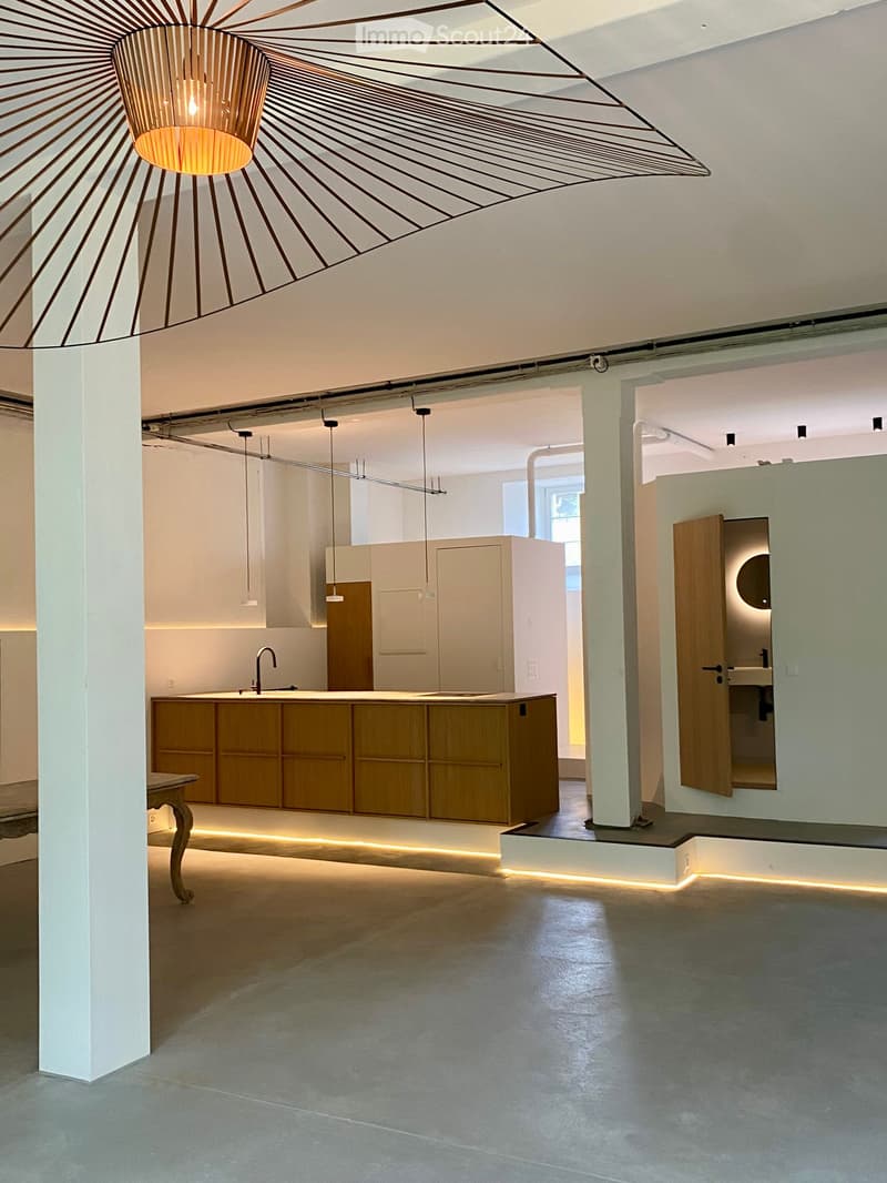 Open-plan space with a modern kitchen island, sink, faucet, and cabinets, illuminated by pendant lights and a geometric chandelier.