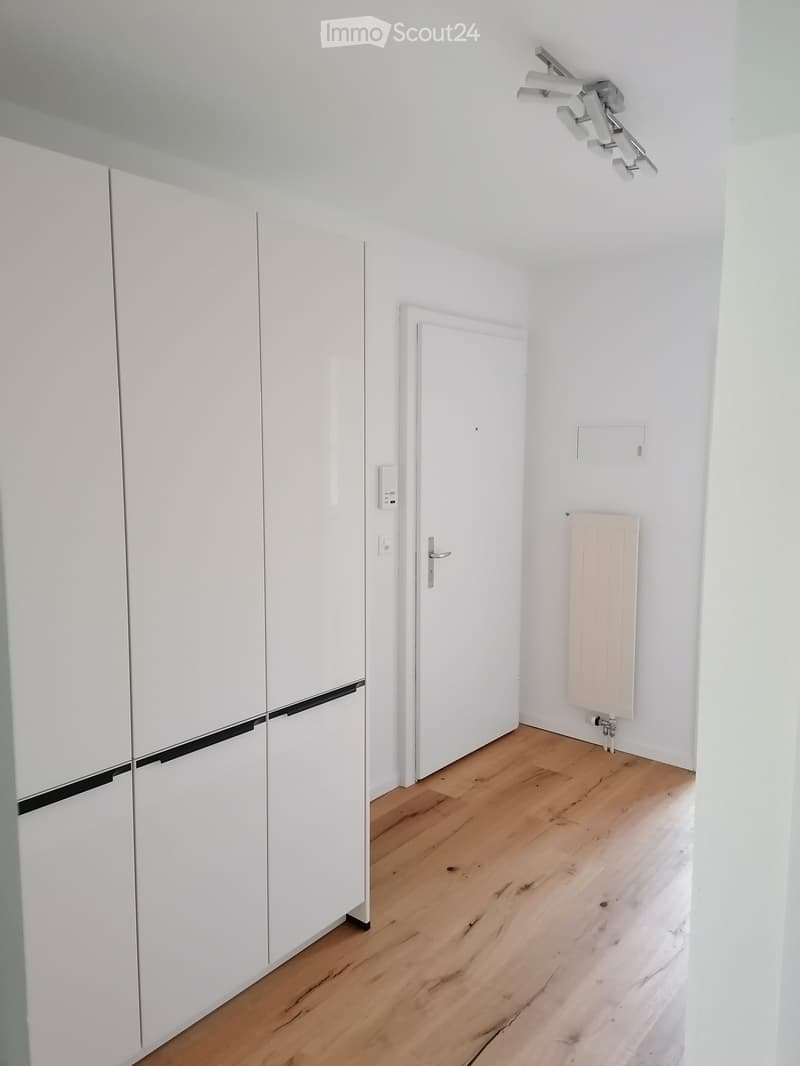 Empty room with white walls, wooden floor, white closet, radiator, and a door.
