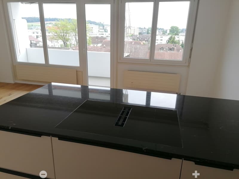 Modern kitchen with black countertop, integrated sink, and large windows offering a view of the cityscape.