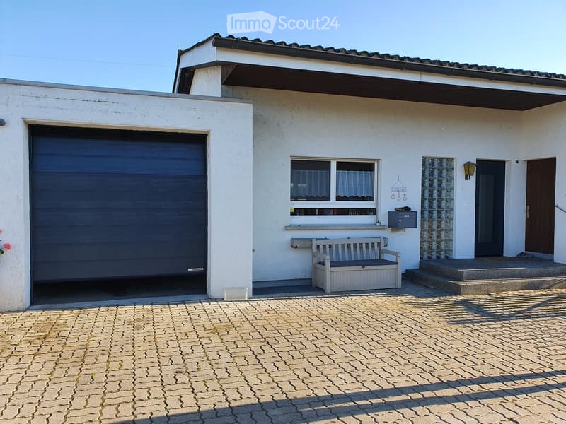 Two-story house with a garage, white exterior, and a small bench near the entrance.