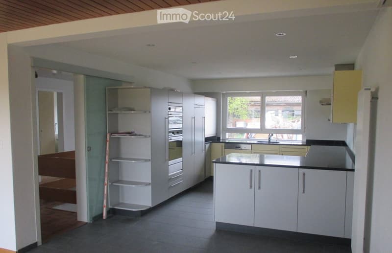 Modern kitchen with white cabinets, stainless steel appliances, and a black countertop. Features a large window with a view of the garden.