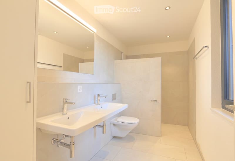 Modern bathroom with double sink, chrome faucets, toilet, large mirror, and recessed lighting.