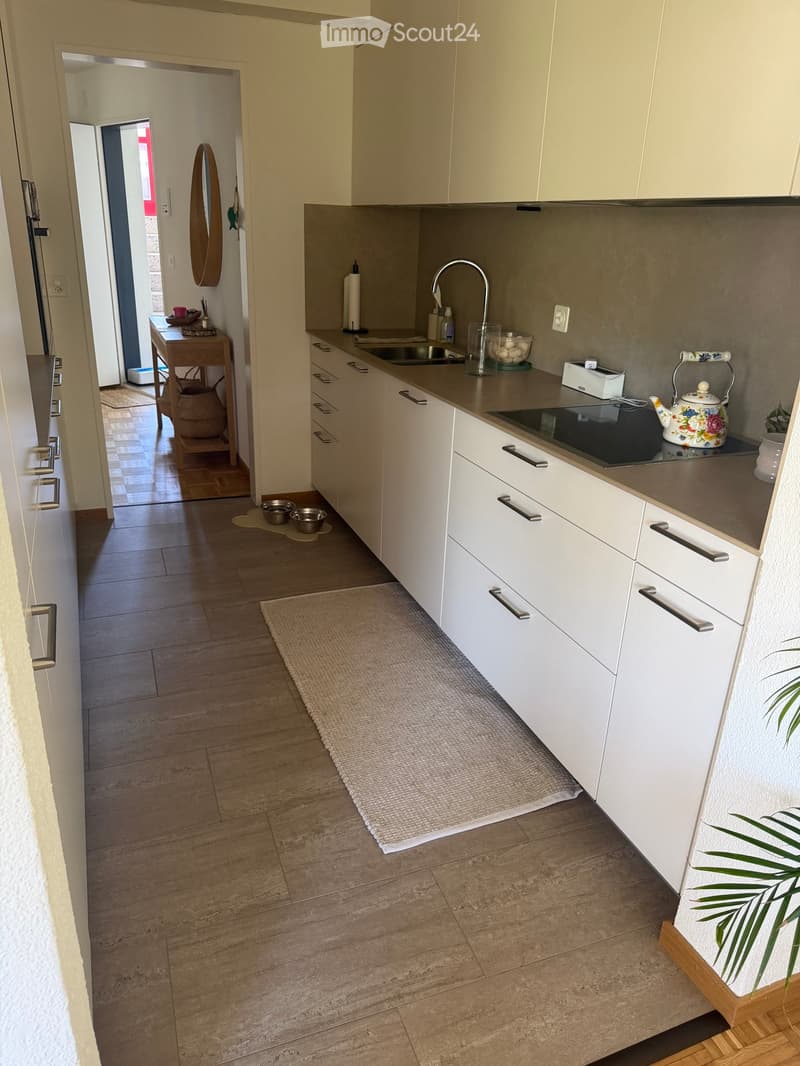 Modern kitchen with white cabinets, stainless steel sink, induction stove, and a small table in the adjacent area.