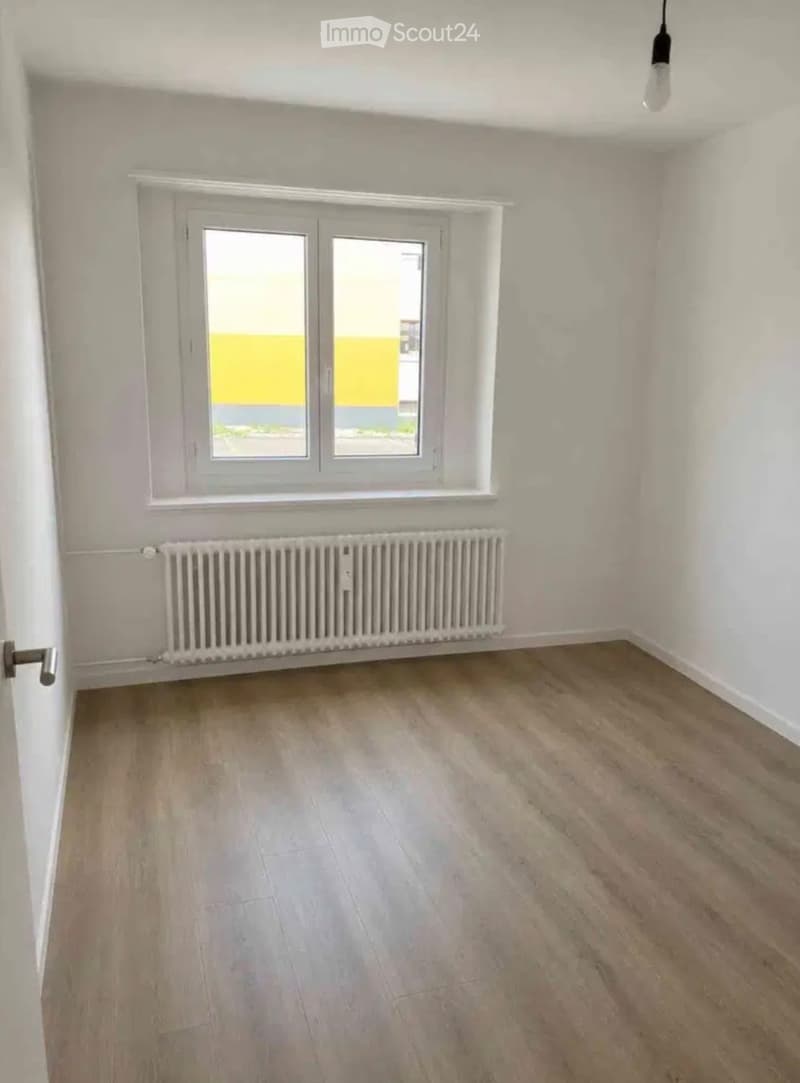 Empty room with light wooden flooring, white walls, a window with double glass panes, and a radiator below the window.