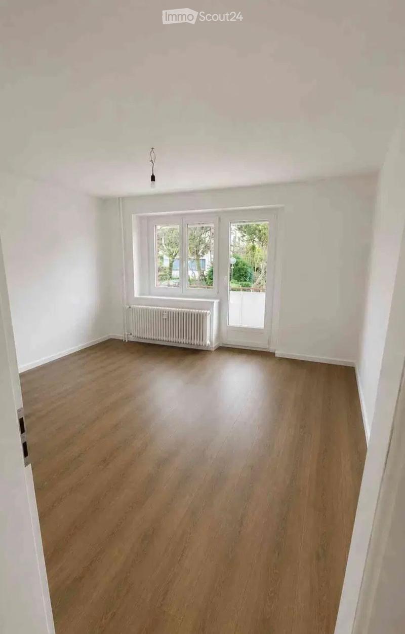 Empty room with wooden flooring, white walls, large windows, and a radiator. No furniture or equipment present.
