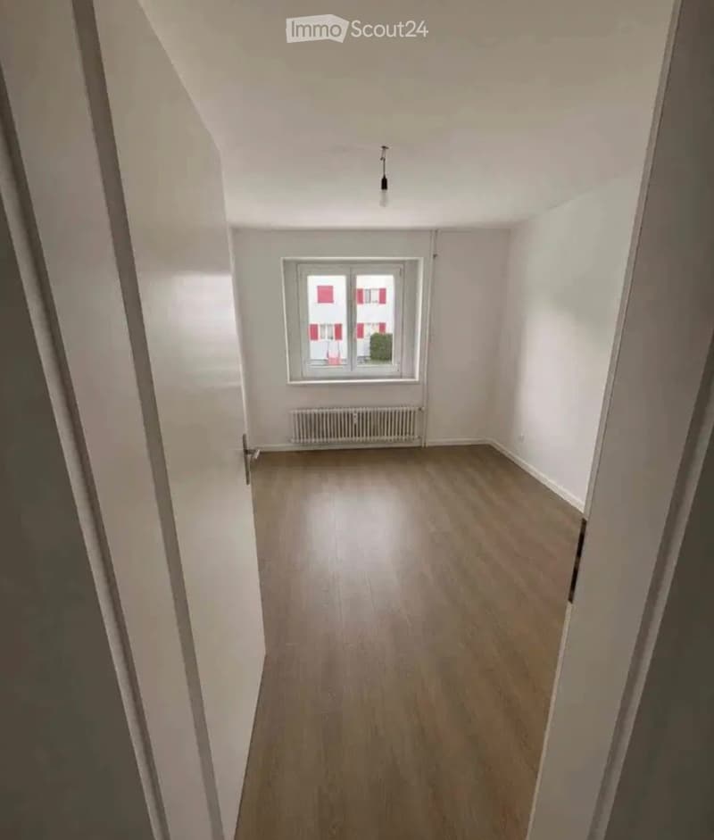 Empty room with wooden flooring, white walls, a single window, and a radiator below it. No furniture or personal items are present.