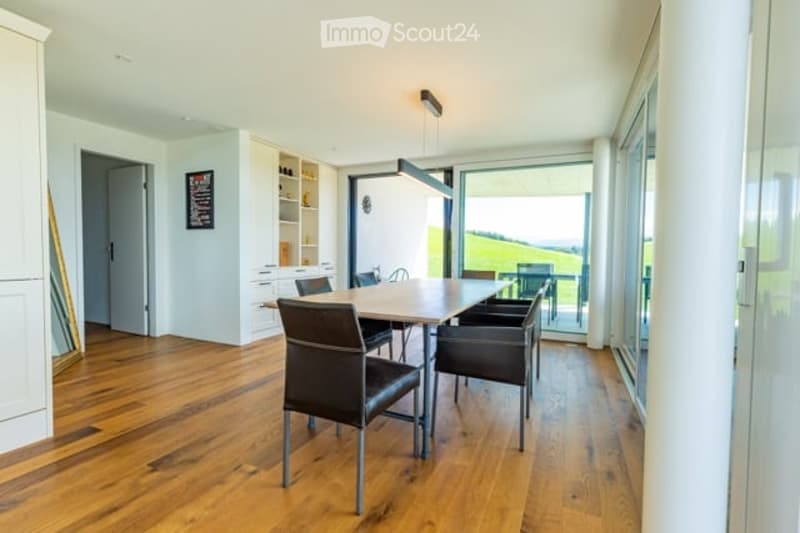 Bright dining area with wooden flooring, modern dining table and chairs, built-in cabinetry, pendant light fixture, and large windows offering a scenic view.