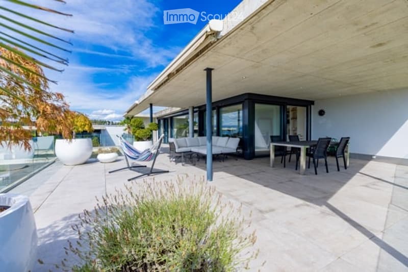 Modern outdoor patio with a covered seating area, white furniture, and a dining set, surrounded by plants and a scenic view.