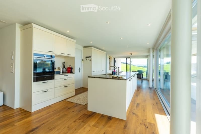 Modern kitchen with white cabinets, wooden flooring, island, and large windows offering a view.