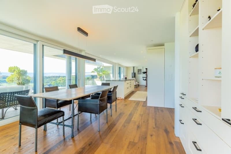 Bright dining area with a modern wooden dining table and chairs, large windows offering a scenic view, and built-in white cabinetry.