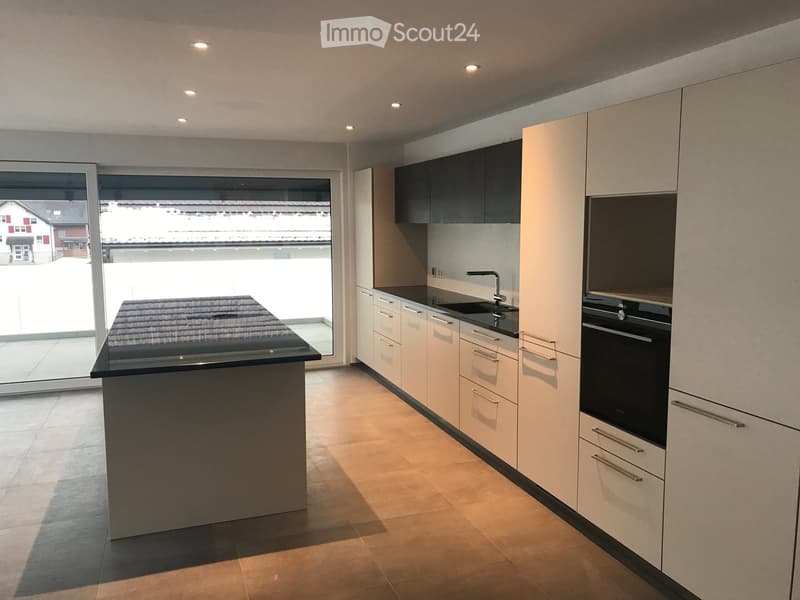Modern kitchen with light-colored cabinets, a black countertop island, and built-in appliances including an oven and sink.