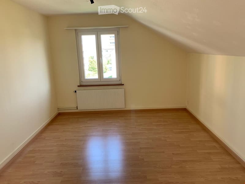 Empty room with wooden flooring, light-colored walls, a window with white frames, and a radiator below the window.