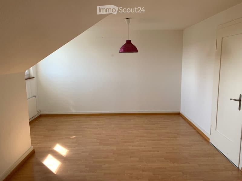 Empty room with wooden flooring, white walls, and a single hanging lamp. No furniture or personal items are present.